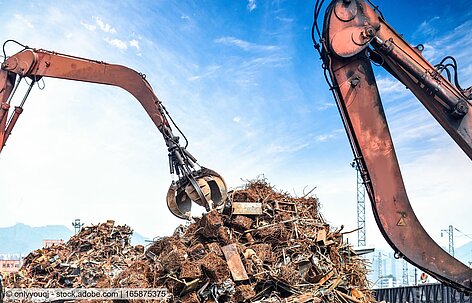 Two material handlers and a heap of obsolete scrap in a recycling yard, seen against the sky.