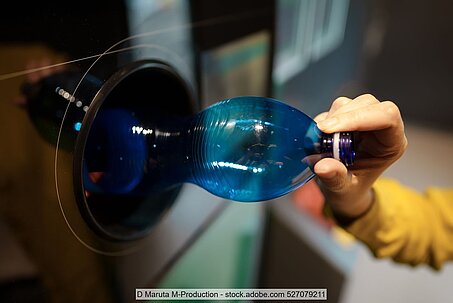 Hand places a single-use PET bottle in a reverse vending machine