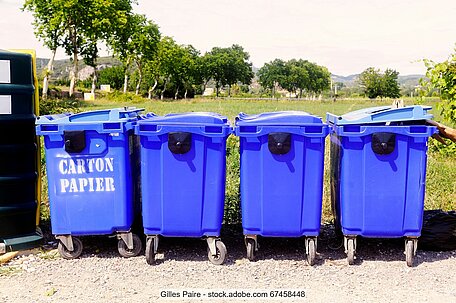 A row of four blue 4-wheeled collection bins for recovered paper and board in a French recycling yard