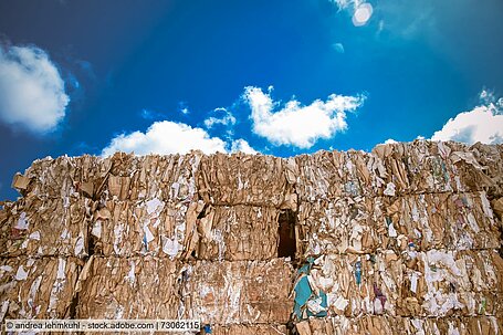 Stacked bales of waste paper against a blue, slightly cloudy sky 