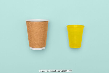 a paper cup lies next to a yellow plastic cup against an robins egg blue background