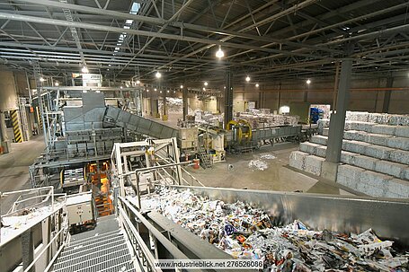 View of the interior of a sorting plant for recovered paper, with conveyors, sorting units and stacked bales of sorted paper for recycling.