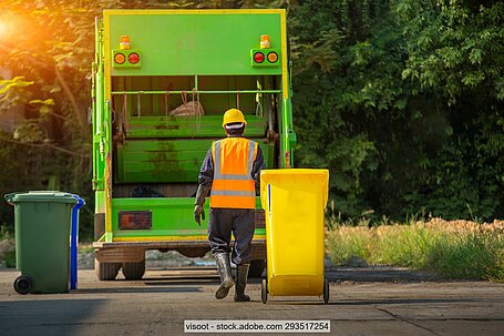 Bin man carrying out waste collections with yellow waste standing in front of waste collection vehicle