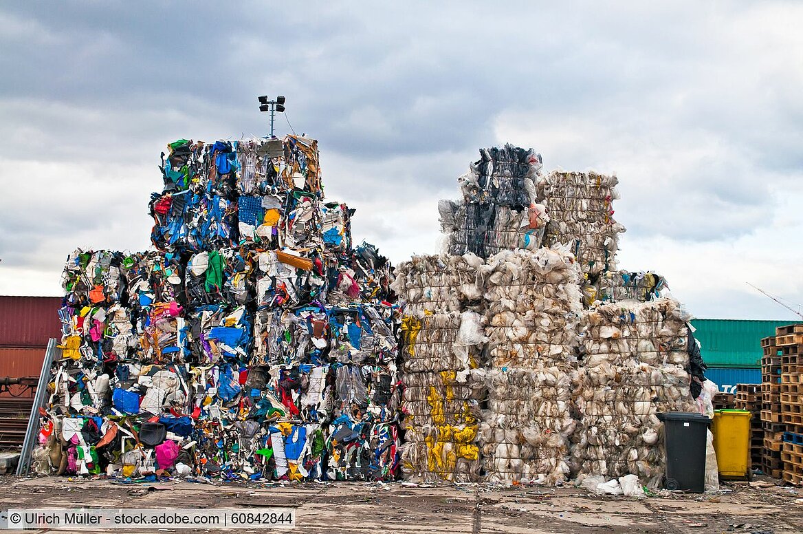 Two stacks of baled waste plastics in a yard. The stock on the left contains mixed colours, the one on the right white, natural and yellow material. 