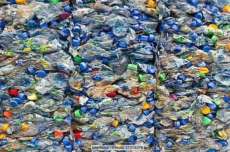 Stacked bales of post-consumer PET bottles in mixed colours, predominantly blue and green.