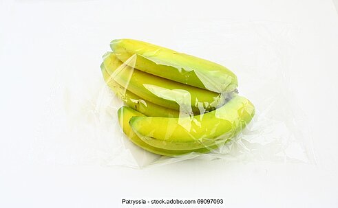 Stock photo of a bunch of bananas wrapped in a clear plastic bag lying in a white surface.