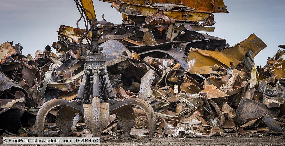 Heap of ferrous scrap in a yard with the grab claw of a materials handler in front of it