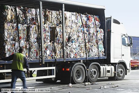 Open curtainsider lorry with waste bales stacked on its bed 