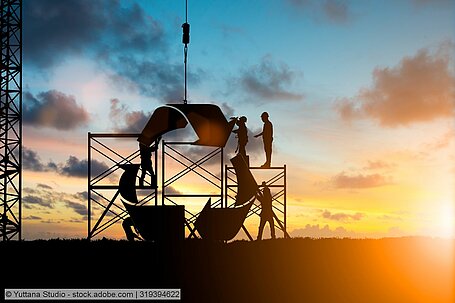 stock photo, workers assemble a structure in the shape of the chasing arrows symbol against a sunset