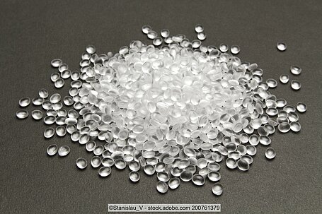 Transparent plastic pellets on a dark surface.