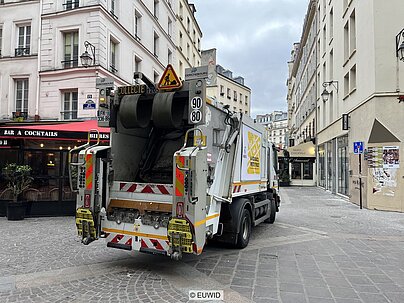 Waste collection truck on street between two restaurants in Paris city centre