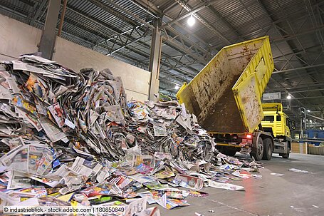 Tipper lorry unloading recovered paper inside industrial building.