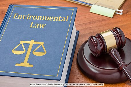 A book with the title "Environmental Law" lies on a desk next to a judge's gavel. 
