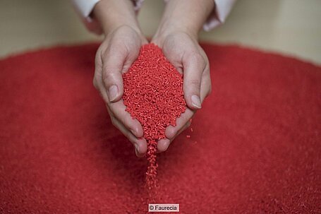 Two hands holding red plastic pellets.