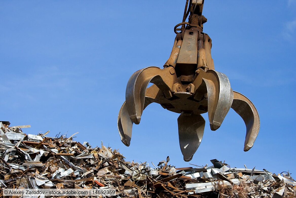 Stock photo of a material handler's opened claw grab above a heap of obsolete scrap. 