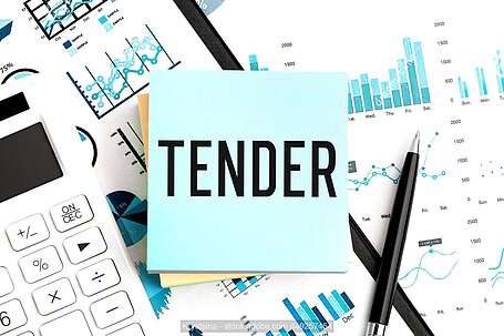 the word tender in black text on a light blue note paper, with pencils, charts and a calculator in the backgroun