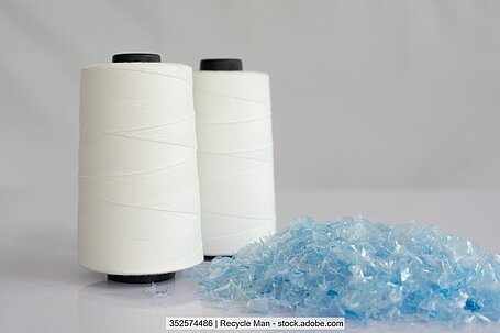 Photo showing clear blue PET flakes and two bobbins of white polyester yarn.