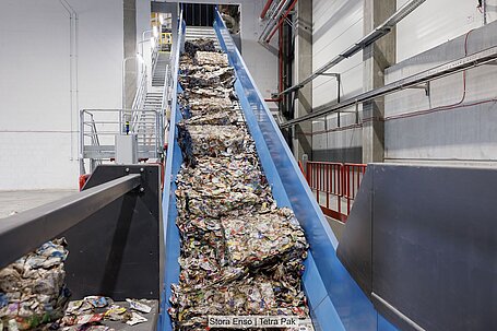 Baled post-consumer beverage cartons on a conveyor transporting them to the repulping line.