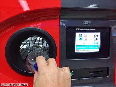 Man's hand places an empty PET bottle in to a reverse vending machine