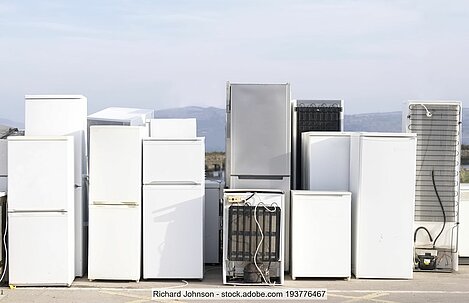 Row of end-of-life refrigerators and freezes standing in a yard. 