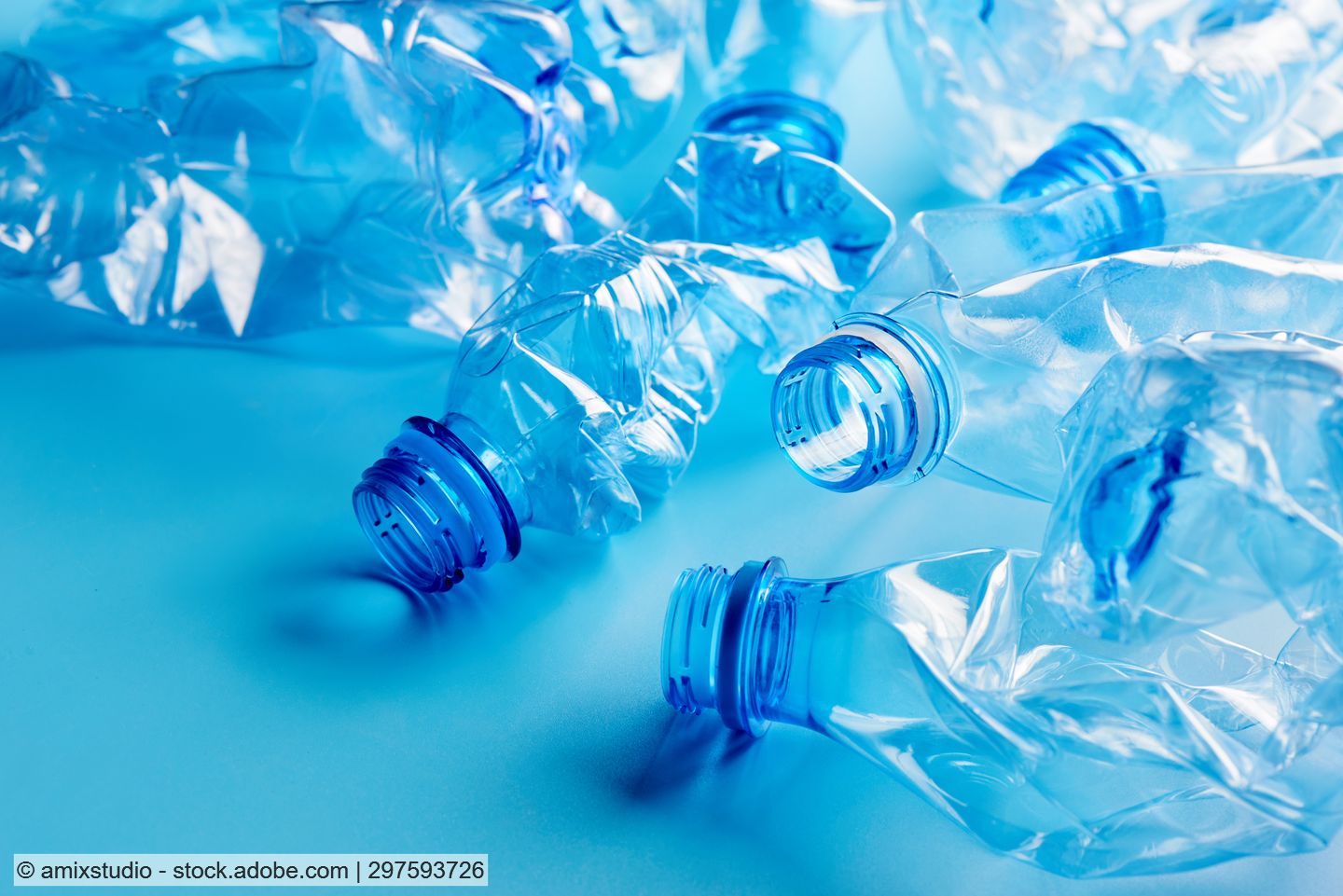 Clear crushed PET bottles lie scattered against a light blue background