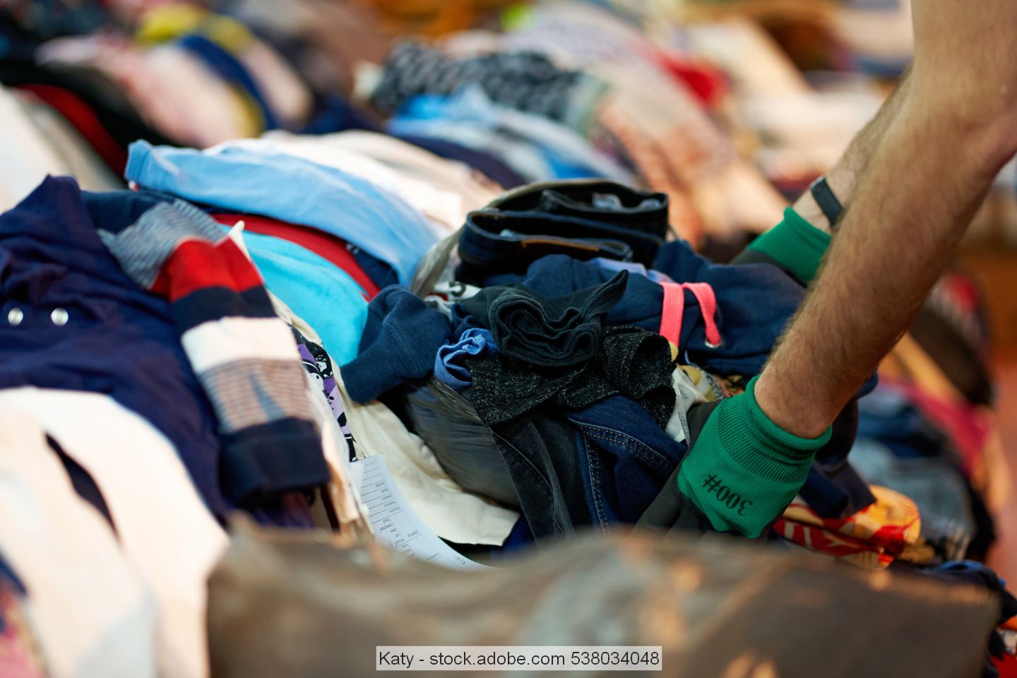Man wearing workgloves sorts through piles of used clothing
