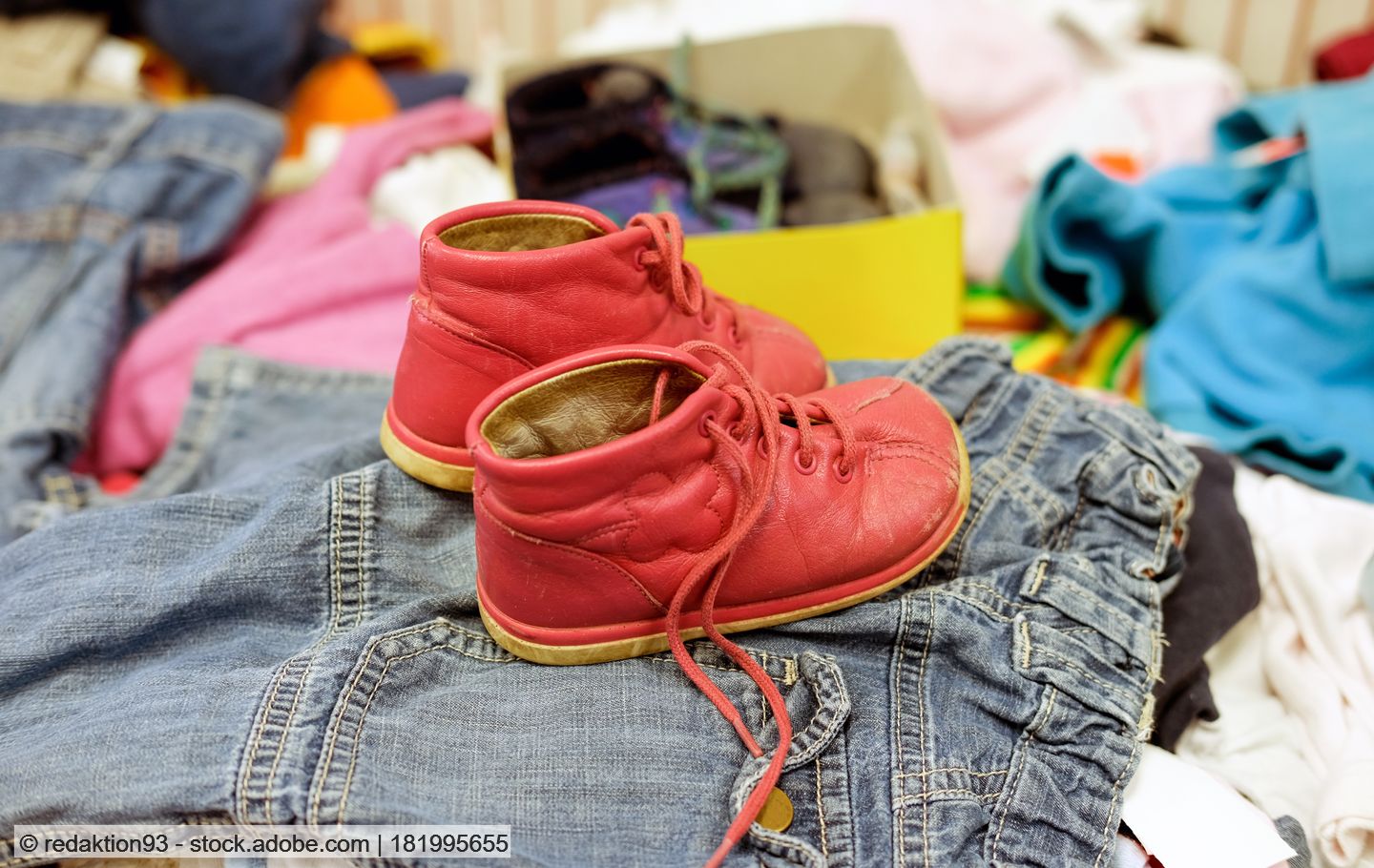A pair of red baby shoes stand on top of a pile of second hand clothes