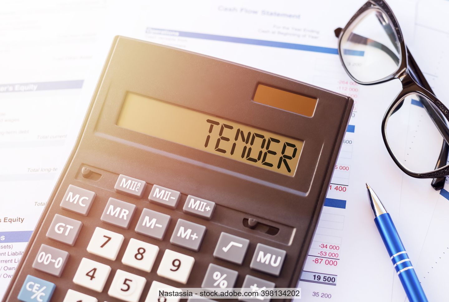 Word "tender" on a calculator display, lying atop financial projections with reading glasses and a pen