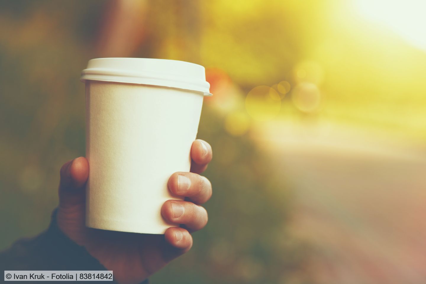 Hand holding a disposable coffee cup with a plastic lid