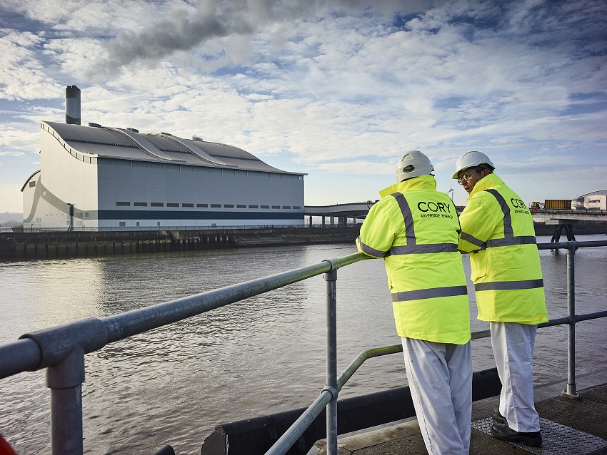 Two Cory employees in hi-vis jackets stand opposite the Riverside 1 Efw facility in London