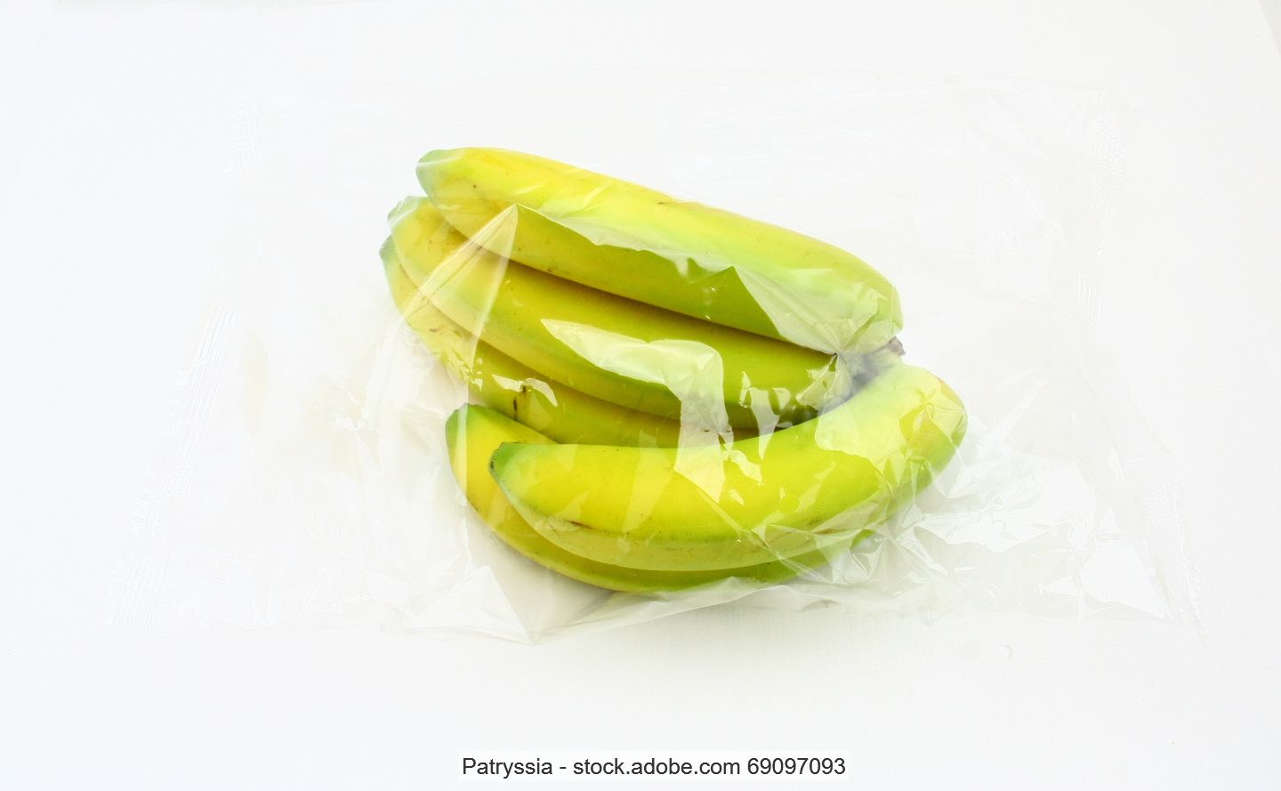 Stock photo of a bunch of bananas wrapped in a clear plastic bag lying in a white surface.