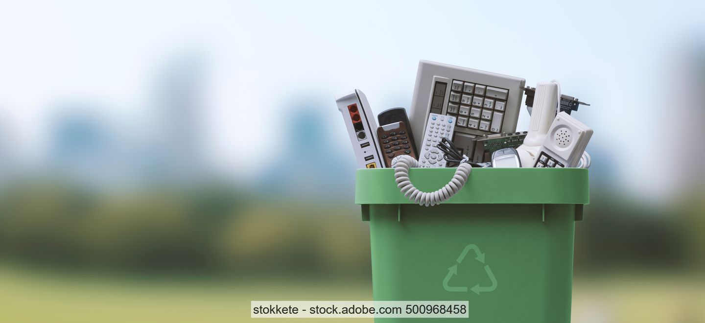Various small electronic and electrical appliances in a green waste bin with the "chasing arrows" recycling symbol.