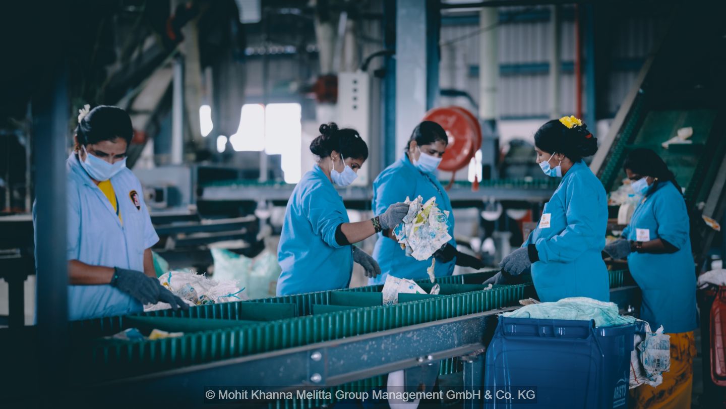 Women in blue work coats sorting plastics at a conveyor belt.