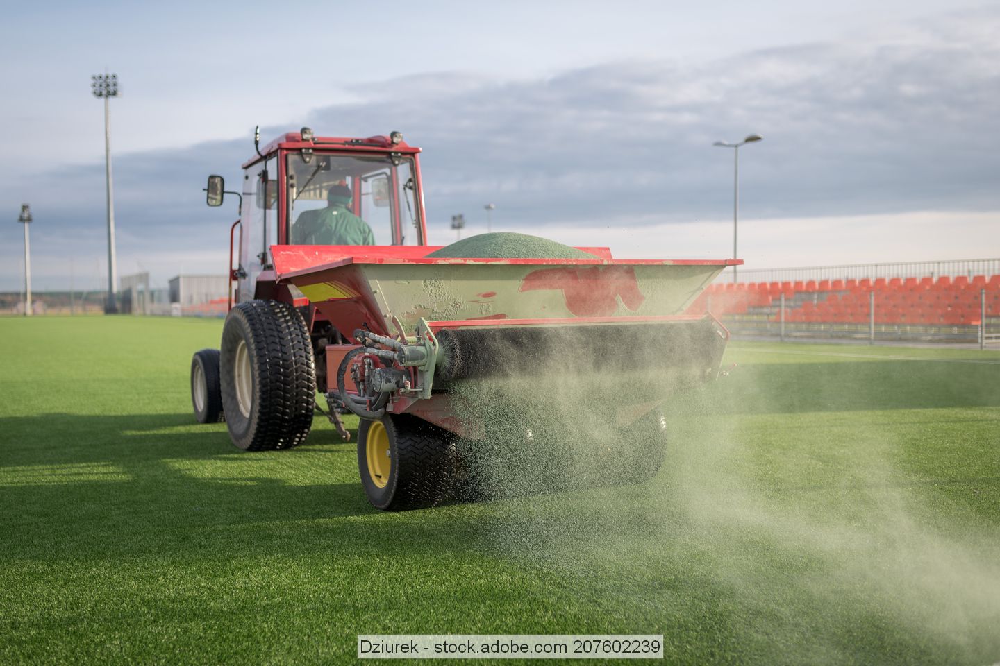 A spreader spreads infill material on artificial turf sports field. 