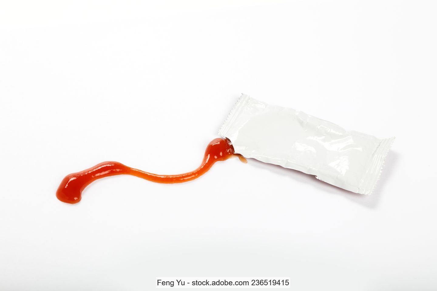 Single ketchup portion in an opened white plastic sachet.