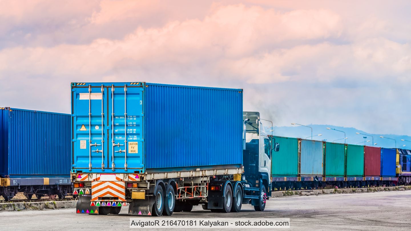 Lorry carrying a container standing next to a freight train.