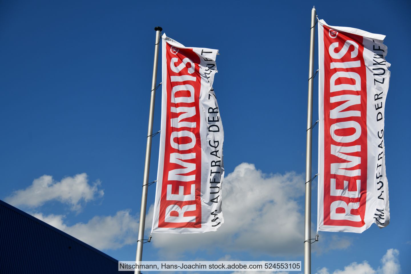 Two red and white Remonids flags with the company logo and tagline  in front of a slightly cloudy sky