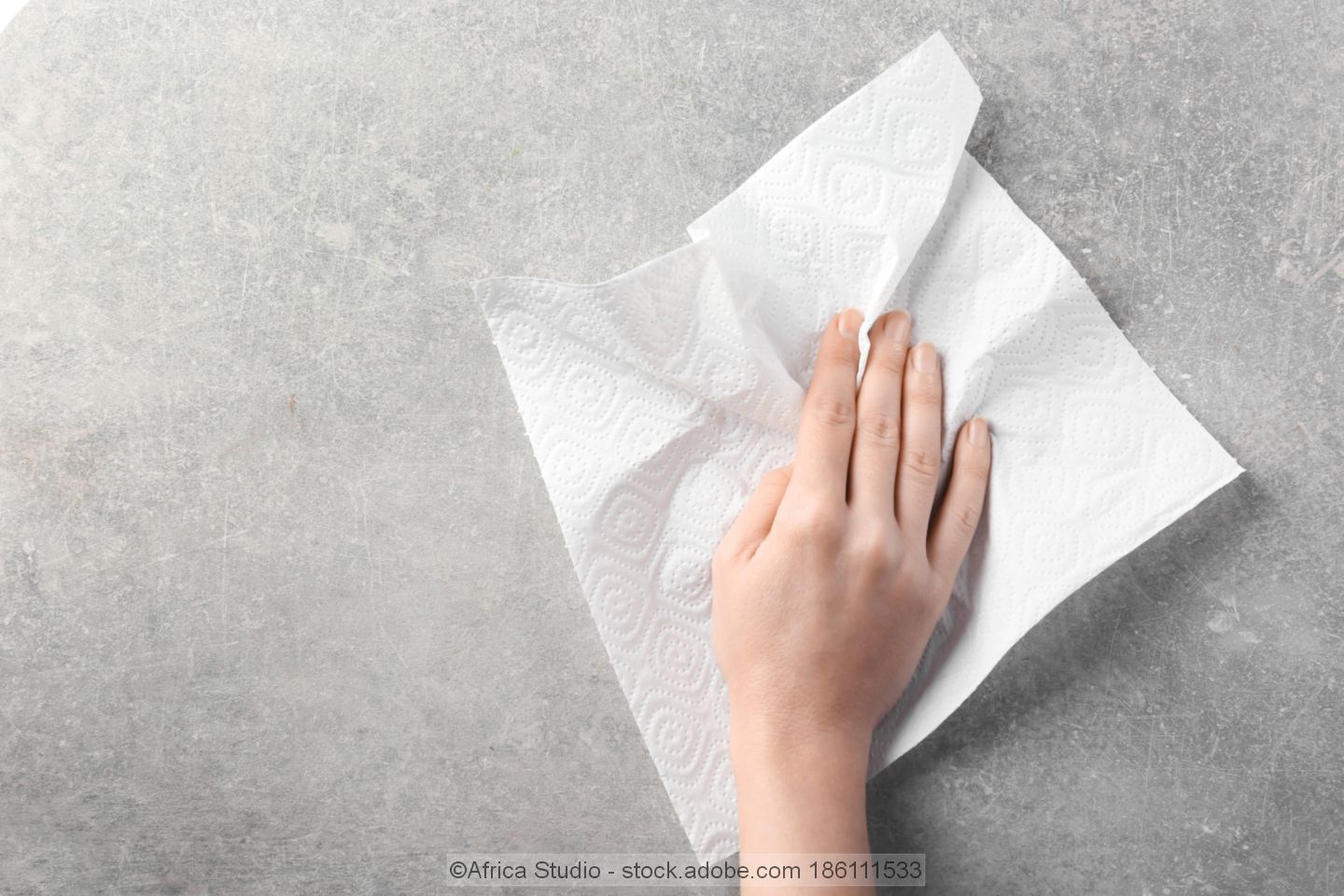Hand wiping a grey surface with a paper towel