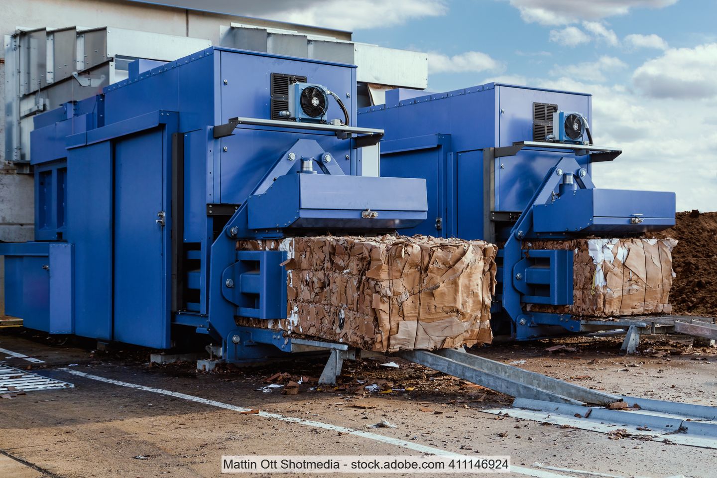 Two blue baling presses in a yard with OCC bales